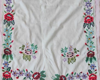 Puede incluir: Textil de lino blanco con bordados florales coloridos. El bordado presenta flores y hojas rojas, moradas, azules y verdes. Los bordes están adornados con un delicado encaje blanco.