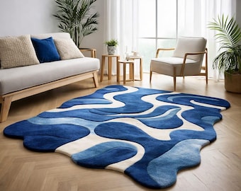 May include: A blue and white abstract area rug with a wavy design. The rug features shades of blue and white, creating a flowing pattern. The rug is placed on a wooden floor in a living room setting.