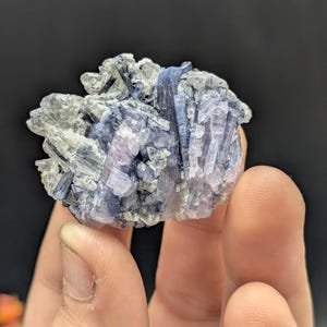 May include: A cluster of blue and white crystals. The crystals have a layered appearance, with some sections appearing more translucent than others. The overall shape is irregular, with sharp edges and points. The color palette includes shades of blue, white, and hints of lavender.