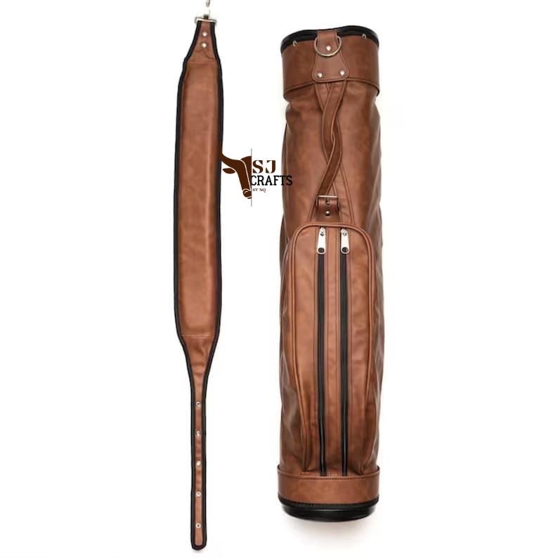 May include: A brown leather golf bag with a matching shoulder strap. The bag has two vertical zippered pockets and a handle. The shoulder strap is long and adjustable. The bag has the text "SJ Crafts" on it.