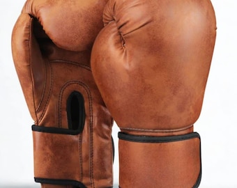 May include: A pair of brown boxing gloves with black trim. The gloves are made of a textured material and have a classic design. The wrist straps are secured with a hook-and-loop closure. The gloves are designed for boxing and other combat sports.