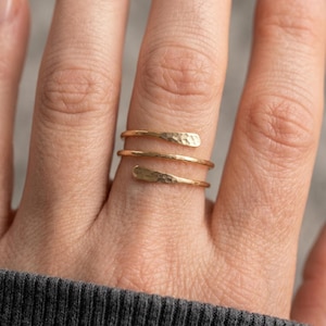 Peut inclure: Une bague bypass dorée présentant un design en spirale qui s'enroule autour du doigt. L'anneau en métal possède une finition martelée texturée et se termine par deux extrémités aplaties et légèrement effilées sur le devant du doigt.