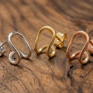 May include: Three stud earrings in silver, gold, and rose gold tones, each featuring a continuous, curved, open-loop design. Each earring includes a post back with a butterfly clutch stamped with 925, indicating sterling silver construction.