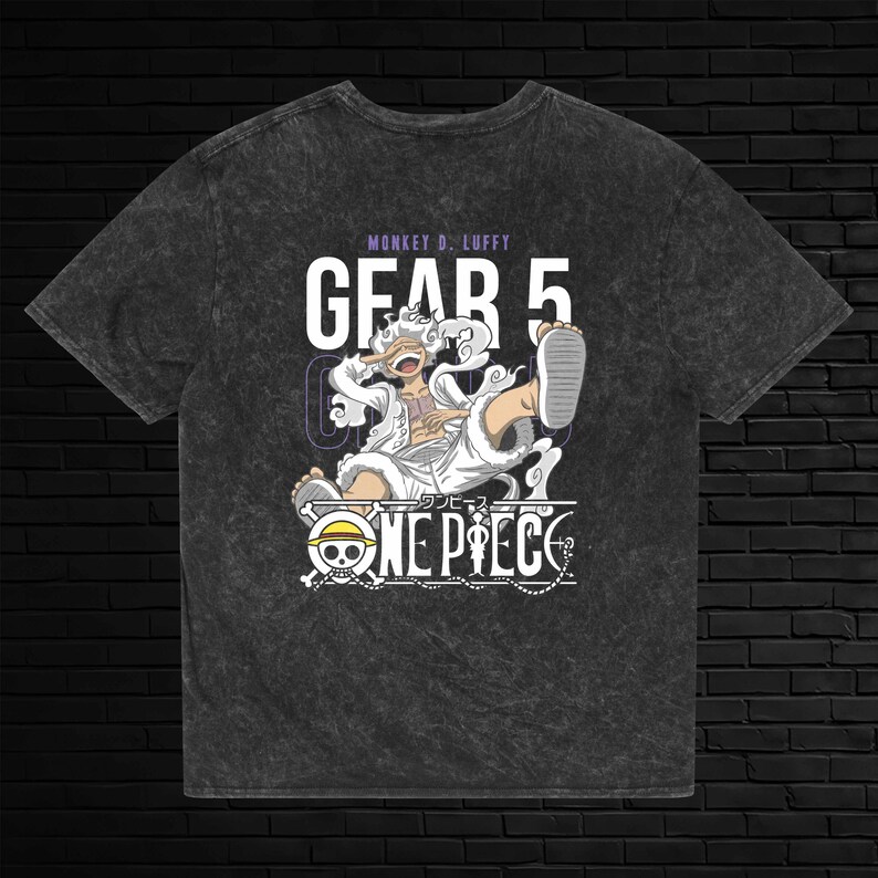 May include: A charcoal grey acid-wash t-shirt featuring a graphic of Monkey D. Luffy in Gear 5 form. The design includes the text "MONKEY D. LUFFY", "GEAR 5", and the "ONE PIECE" logo with a skull and crossbones emblem in white and black.