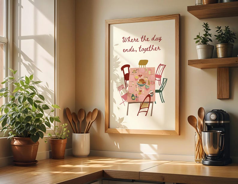 Puede incluir: Una impresi&oacute;n enmarcada con el texto "Where the day ends, together" sobre una colorida ilustraci&oacute;n de una mesa de comedor preparada para una comida. La impresi&oacute;n est&aacute; en un marco de madera clara. La imagen est&aacute; en un entorno de cocina con plantas y utensilios de madera.