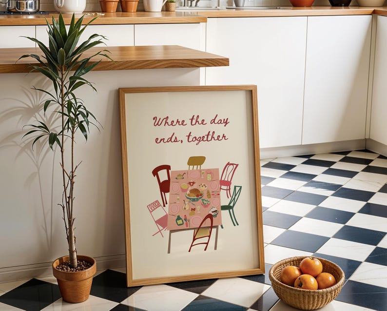 Puede incluir: Una impresi&oacute;n enmarcada con el texto "Where the day ends, together" presenta una ilustraci&oacute;n de mesa con sillas. Una planta en maceta y una cesta de naranjas est&aacute;n cerca. El suelo tiene un patr&oacute;n de cuadros blancos y negros.
