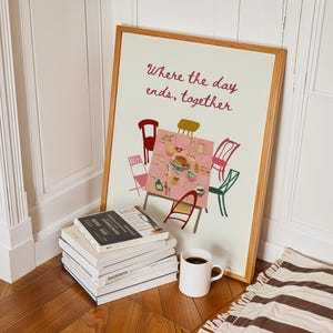Puede incluir: Una impresi&oacute;n art&iacute;stica enmarcada con el texto "Where the day ends, together". La impresi&oacute;n representa una mesa con sillas. Una pila de libros y una taza blanca con caf&eacute; est&aacute;n frente a la impresi&oacute;n. Una alfombra a rayas est&aacute; en el suelo.