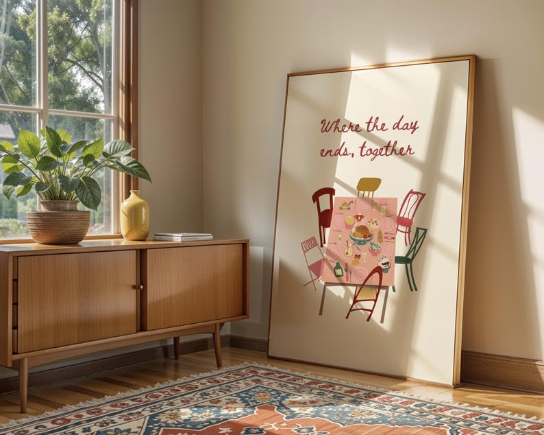 Puede incluir: Una impresi&oacute;n art&iacute;stica enmarcada que presenta una escena de mesa de comedor con sillas de varios colores. El texto "Where the day ends, together" se muestra en cursiva. La obra de arte est&aacute; apoyada contra una pared cerca de un mueble de madera y una ventana.