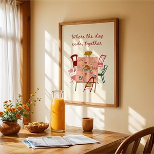 Puede incluir: Una impresi&oacute;n enmarcada con el texto "Where the day ends, together" sobre una colorida ilustraci&oacute;n de una mesa. Una botella de vidrio de jugo de naranja, un peque&ntilde;o jarr&oacute;n marr&oacute;n con flores naranjas y una mesa de madera est&aacute;n en primer plano.