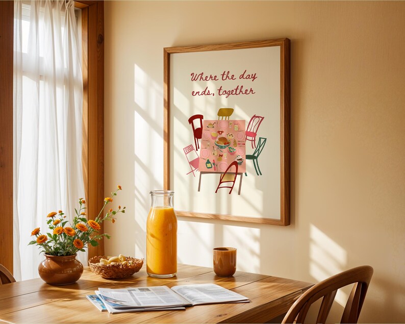 Puede incluir: Una impresi&oacute;n enmarcada con el texto "Where the day ends, together" sobre una colorida ilustraci&oacute;n de una mesa. Una botella de vidrio de jugo de naranja, un peque&ntilde;o jarr&oacute;n marr&oacute;n con flores naranjas y una mesa de madera est&aacute;n en primer plano.