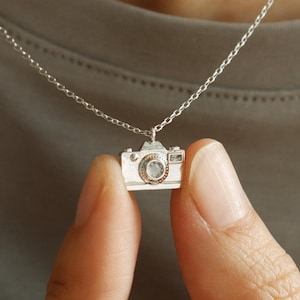 May include: A white ceramic mug with a black handle and the text "But First, Coffee" in a bold, black font. The mug is filled with a dark liquid, likely coffee, and sits on a light-colored surface.