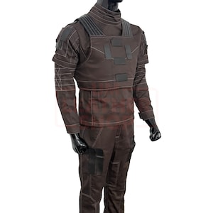May include: A brown tactical uniform, featuring a high-neck top and matching pants. The outfit includes a chest rig with black accents and multiple pockets. White stitching details the seams. The mannequin's arms are bent at the elbows.