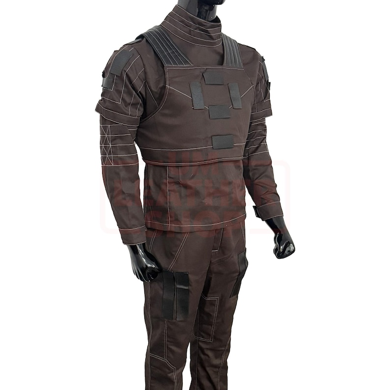 May include: A brown tactical uniform, featuring a high-neck top and matching pants. The outfit includes a chest rig with black accents and multiple pockets. White stitching details the seams. The mannequin's arms are bent at the elbows.