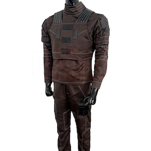 May include: A brown tactical jumpsuit with a high collar, long sleeves, and matching pants. The outfit features black accents on the chest, shoulders, and pockets, with visible stitching details. The mannequin is wearing black gloves.