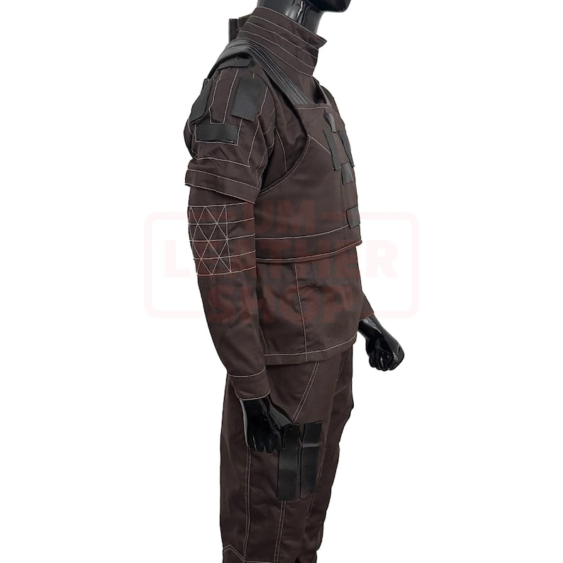 May include: Brown tactical uniform with black accents, displayed on a mannequin. The outfit features a high collar, shoulder pads, and multiple pockets. White stitching details the seams and geometric patterns on the sleeves. The uniform is designed for functionality and durability.