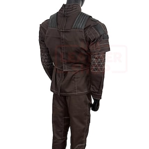 May include: Brown costume with white stitching and black accents. The outfit includes a jacket with a high collar and shoulder pads, and matching pants. The sleeves have a geometric pattern. The costume is displayed on a mannequin.