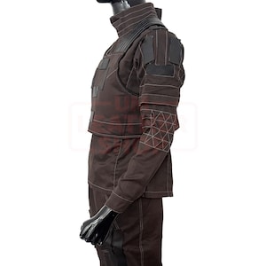 May include: A brown tactical outfit with a high collar, shoulder pads, and a vest-like top. The outfit features white stitching and geometric patterns on the sleeves. The mannequin is wearing a black head covering.