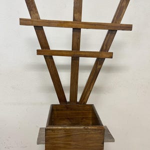 May include: A wooden planter with a trellis design. The planter box is rectangular and stained a dark brown. The trellis features vertical and horizontal wooden slats, creating a decorative structure. The planter is designed for outdoor use.