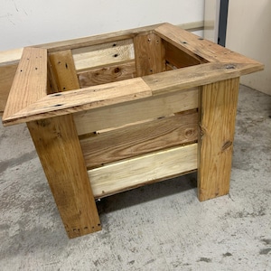May include: A handcrafted wooden planter box made from reclaimed wood. The box has a rectangular shape with a sturdy frame and legs. The natural wood tones and visible grain add to its rustic charm. Perfect for indoor or outdoor use.