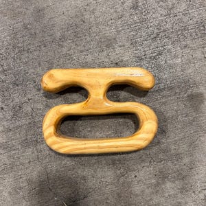 Könnte beinhalten: Ein hellfarbener Holzgriff mit abgerundeter Oberseite und einer ovalen Öffnung. Der Griff besteht aus hellfarbenem Holz mit sichtbaren Maserungsmustern. Der Griff ist für einen einfachen Griff konzipiert.