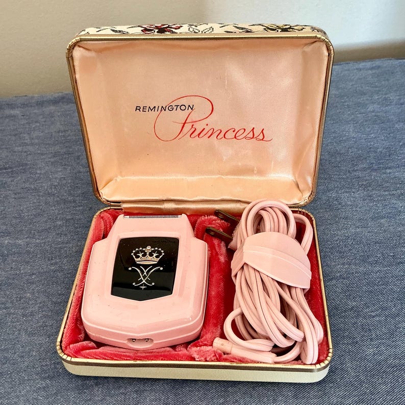 Pu&ograve; includere: Rasoio elettrico Remington Princess rosa vintage nella sua custodia originale. Il rasoio ha un pannello nero con un disegno a corona. La custodia &egrave; foderata in raso rosa e velluto rosso. Il cavo &egrave; anch'esso rosa.