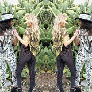 May include: Two people wearing sequined tops and patterned pants pose in front of a cactus garden. One person is wearing a black top with gold sequins and black pants with a floral pattern. The other person is wearing a silver top with white sequins and white and black striped pants.