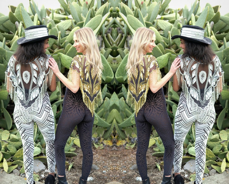 May include: Two people wearing sequined tops and patterned pants pose in front of a cactus garden. One person is wearing a black top with gold sequins and black pants with a floral pattern. The other person is wearing a silver top with white sequins and white and black striped pants.