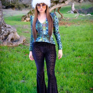 Peut inclure: Une femme portant un chapeau en fourrure blanche, une veste &agrave; motifs bleus et verts et un pantalon en velours noir &agrave; pattes d'&eacute;l&eacute;phant. Elle se tient dans un champ herbeux.