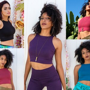 May include: Five women wearing different colored crop tops. The tops are sleeveless and have a high neckline. The women are wearing different colored pants and skirts.