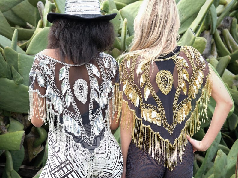 May include: Two women wearing black sheer shawls with gold and silver sequins and fringe. The shawls are decorated with leaf and floral patterns.