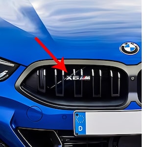 May include: Close-up of a blue BMW car's front grille. The grille features the text "X6 M" in silver and red. The car has a German license plate and the BMW logo.
