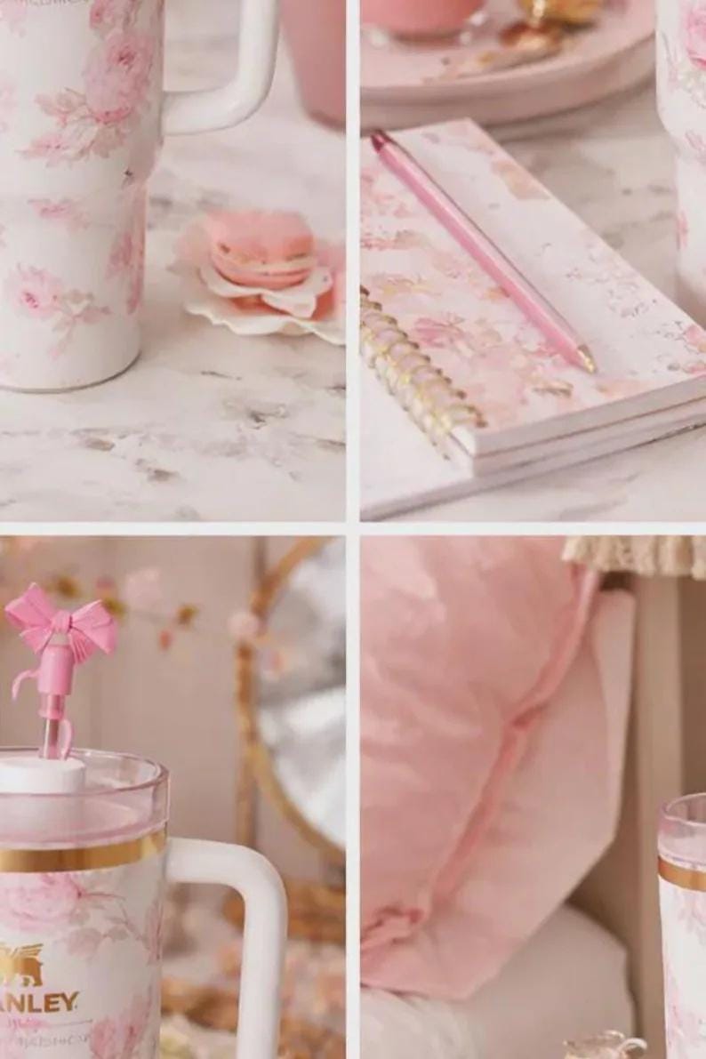 May include: A collection of pink floral-themed items. Includes a tumbler, a notebook with a pen, and a pink bow-topped straw. The tumbler has a white handle and gold accents. A pink macaron sits on a small plate.