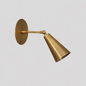 May include: A brass wall sconce with a circular backplate and a conical shade. The shade is adjustable and connected to the backplate by a straight arm. The sconce has a warm, metallic finish.