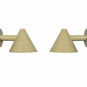 May include: Two beige wall sconces with a conical shade and a circular mounting plate. The sconces have a minimalist design and are mounted on a white background. The shades are approximately 6 inches in height.