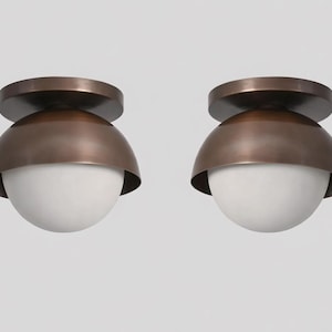 May include: Two bronze-coloured, dome-shaped ceiling lights with a white, spherical glass shade. The lights have a circular base and a rounded top. The fixtures are modern and minimalist.