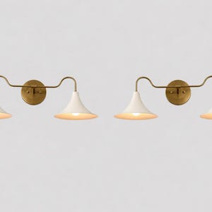 May include: Two wall lights featuring a brass finish and white, cone-shaped shades. Each light has a circular wall mount and a curved arm. The shades are illuminated, emitting a warm glow.