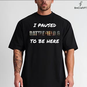 Puede incluir: Camiseta negra con el texto blanco "I PAUSED BATTLEFIELD 6 TO BE HERE". El texto "BATTLEFIELD 6" tiene un diseño gráfico. La camiseta es de manga corta y cuello redondo.