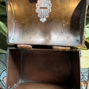 May include: An open, antique-style metal box with a hinged lid. The box is a dark bronze color with a decorative silver-colored clasp. The interior of the box is empty. The box is likely used for storage or display.