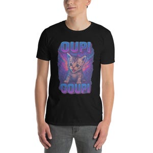 May include: Black t-shirt featuring a cartoon kitten with the text "OUPI GOUPi" in a colorful, stylized font. The kitten is depicted with its mouth open, set against a vibrant, cosmic background.