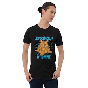 May include: Black t-shirt featuring a cartoon image of an orange cat with the text "LE FECONDEUR D'HOMME" in blue. The cat is sitting with its legs spread, and blue lightning bolts surround the cat.
