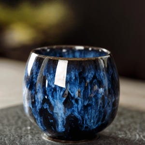 Peut inclure: Une petite tasse ronde en céramique avec une finition brillante. La tasse présente un design marbré bleu et noir saisissant, créant une apparence artistique unique. La tasse est conçue pour les boissons et convient à un usage domestique.