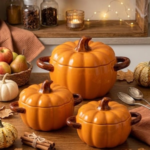 Puede incluir: Tres ollas de cerámica naranja con forma de calabaza, con tapas, tallos y asas de color marrón oscuro. El conjunto incluye una olla grande y dos más pequeñas, todas con un diseño exterior acanalado, dispuestas sobre una superficie de madera.