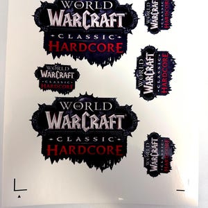 May include: A sheet of stickers featuring the "World of Warcraft Classic Hardcore" logo in various sizes. The logo is predominantly black, white, and red, with a stylized design. The stickers are printed on a white background.