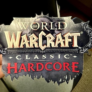 May include: A sticker featuring the "World of Warcraft Classic Hardcore" logo. The logo has a dark background with the words "World of Warcraft" in a stylized font. The word "Hardcore" is in red, and "Classic" is in white.