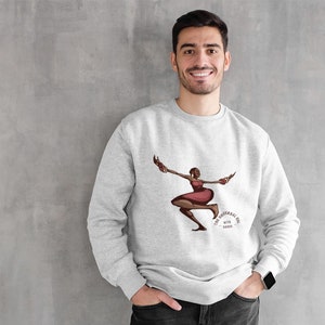 May include: Light gray sweatshirt featuring a graphic of a woman in a red dress with brown accents, holding objects in each hand. The text "THE UNIVERSAL GOD WITH LABBA" is below the graphic. The sweatshirt is worn by a person.