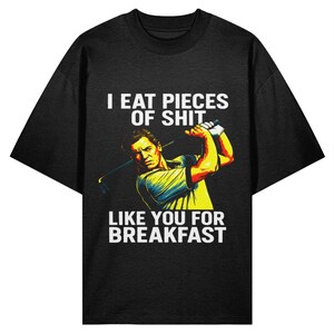 Puede incluir: Camiseta negra con un gráfico de un golfista y el texto blanco "I EAT PIECES OF SHIT LIKE YOU FOR BREAKFAST". El golfista está representado en amarillo, azul y naranja.