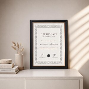 Puede incluir: Un certificado de reconocimiento enmarcado con un marco negro. El certificado tiene bordes decorativos y el texto "Certificado de Reconocimiento" y el nombre del destinatario. El certificado se muestra sobre una superficie blanca.
