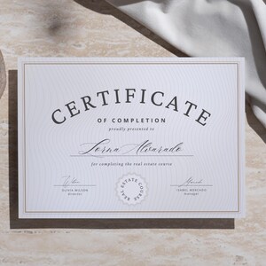 Puede incluir: Un certificado blanco con borde dorado, con el texto "CERTIFICATE OF COMPLETION" y el nombre "Lorna Alvarado". El certificado incluye firmas y un sello del curso de bienes ra&iacute;ces. El fondo es de color beige claro.