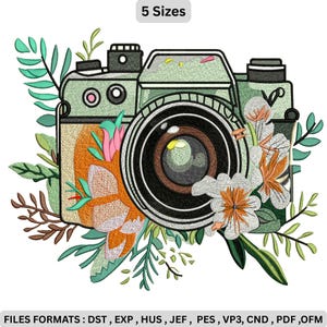 Puede incluir: Diseño bordado de una cámara vintage con detalles florales. La cámara es de color verde claro con una lente marrón y está rodeada de flores blancas y naranjas y hojas verdes. El texto "5 Sizes" está en la parte superior.