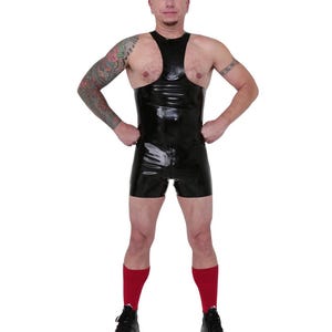 以下が含まれることがあります： ノースリーブのデザインとショートパンツが付いた黒いラテックスボディスーツ。 衣服はジッパーで開閉し、赤い靴下と黒いスニーカーを着用しています。 人は白い背景の前に立っています。